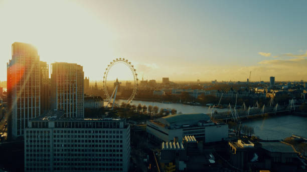 The image shows a stunning sunset view over London, featuring the skyline with the famous Ferris wheel by the river, bathed in golden hues.