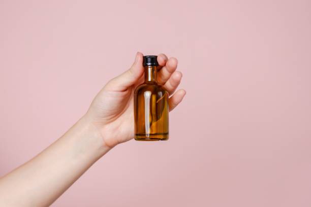 istock Small glass blank bottle mockup in hand on pink background. Package for cosmetics product, nutritional supplements, mixture, alcohol. Space for text 2190656716