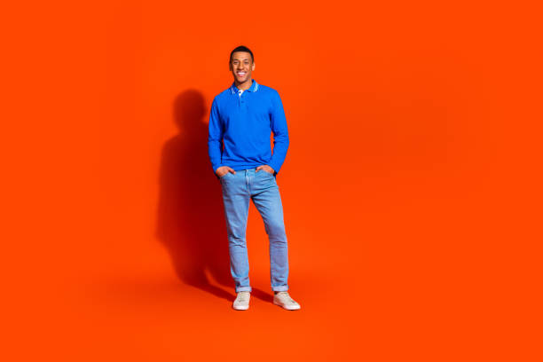 istock Smiling young man in blue shirt standing against vibrant orange backdrop 2190658786