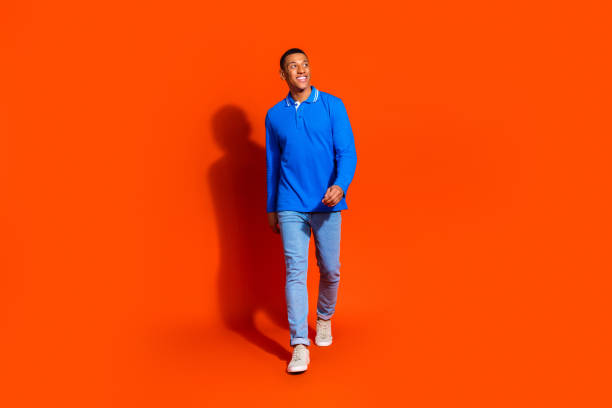 istock Stylish young man confidently strolling against a vibrant orange background 2190658813