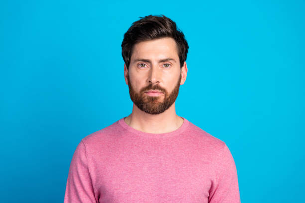 istock Confident bearded man in pink sweater with serious expression on blue background, showcasing modern style and fashion appeal 2190661786