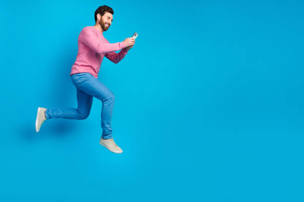 istock Excited young man jumping in air while using smartphone against bright blue background 2190661802