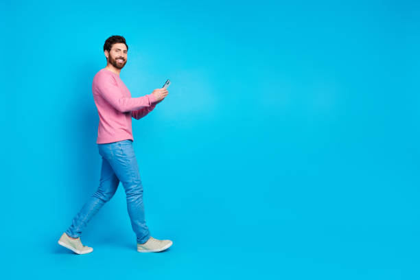 istock Confident man in pink sweater walking with phone against a vibrant blue background 2190661812