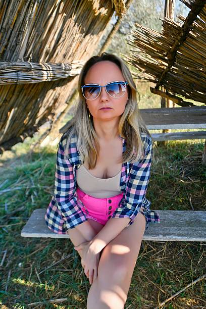 A beautiful woman takes a break from the summer heat in a thatched gazebo on the shore of a lake.