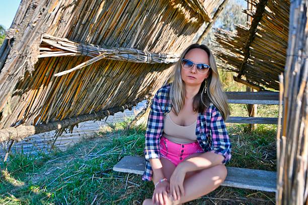 A beautiful woman takes a break from the summer heat in a thatched gazebo on the shore of a lake.