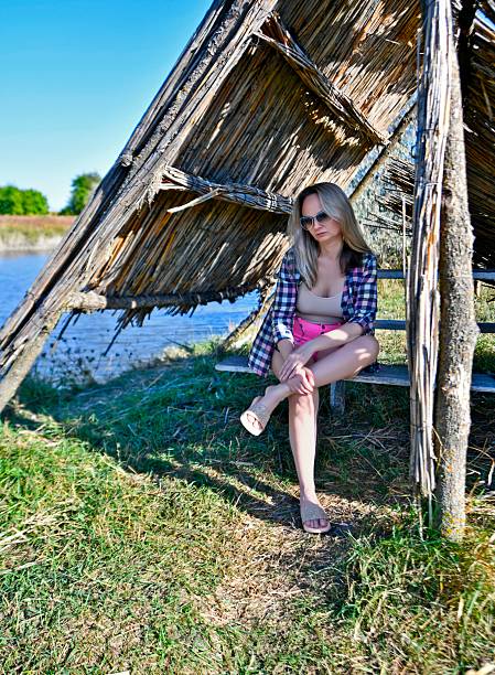 A beautiful woman takes a break from the summer heat in a thatched gazebo on the shore of a lake.