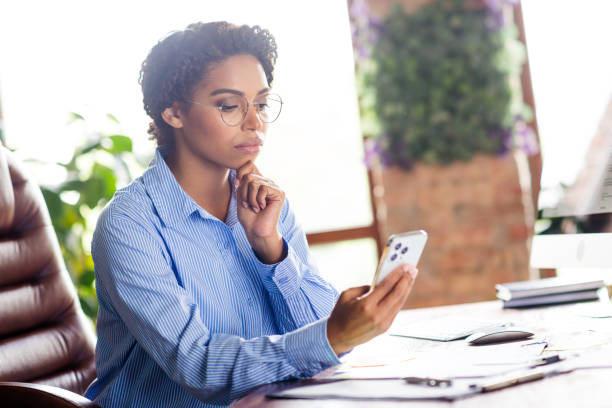 istock Young businesswoman in office setting using smartphone with focused expression, wearing elegant blue blouse 2190665688