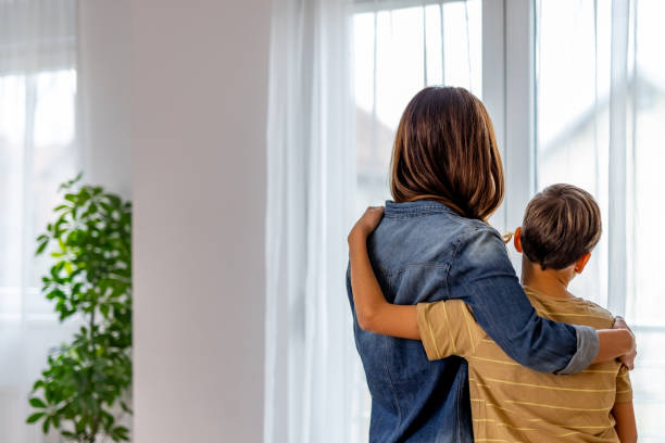 istock Mother hugging son, gazing out home window together, sharing tender moment 2190666572