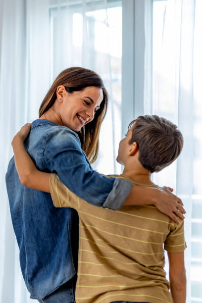 Mother embracing son, sharing warm smile near window, basking in natural light, radiating familial love and happiness