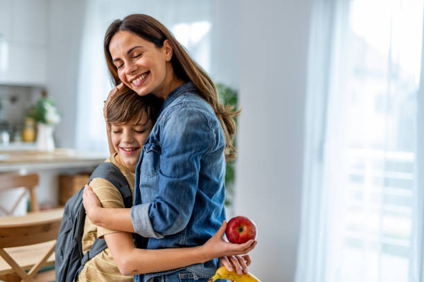 istock Mother hugging her son while holding an apple and a banana, preparing him for a joyful school day filled with love and healthy snacks 2190666631