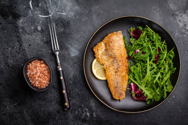 istock Roasted Haddock fish fillet on a plate with salad. black background. top view 2190667113