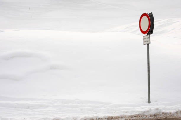 A red and white circular no entry sign standing amidst a vast snow-covered terrain. The sign includes a small additional panel reading 'ecetto veicoli autorizzati,' indicating restricted access. The serene and untouched snowy environment contrasts with the solitary road sign.
