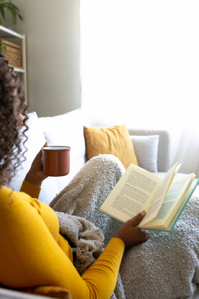 istock Young woman relaxing on sofa reading a book and drinking tea 2190668968