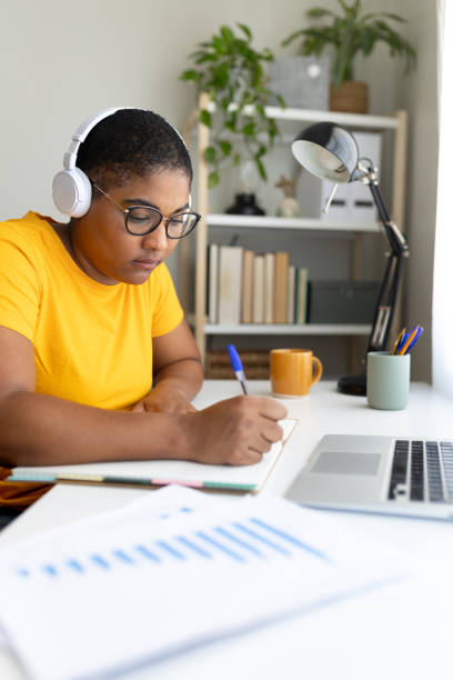 istock Young woman wearing headphones and taking notes while working from home 2190669024