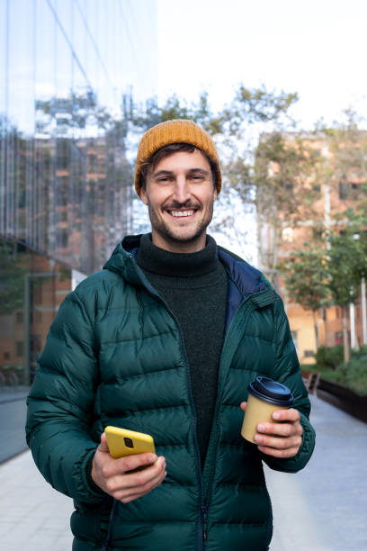 istock Young man using smartphone and holding coffee outside office building 2190669048