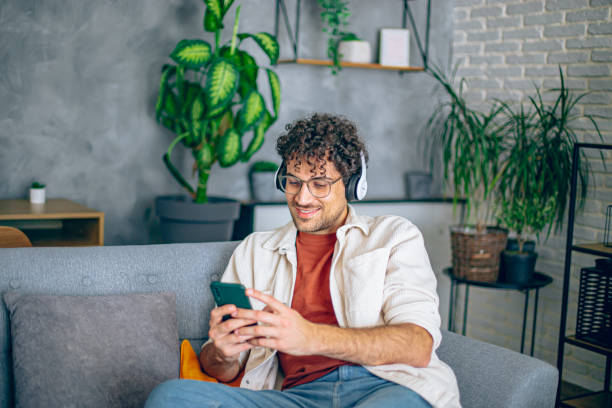 istock Young happy man with headphones using his smartphone while relaxing in the couch at home 2190671400
