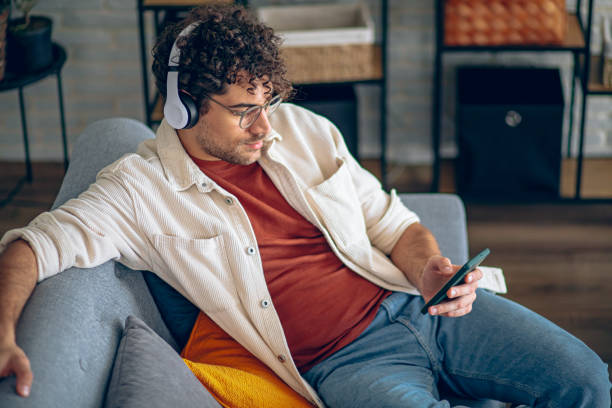 istock Young happy man with headphones using his smartphone while relaxing in the couch at home 2190671853