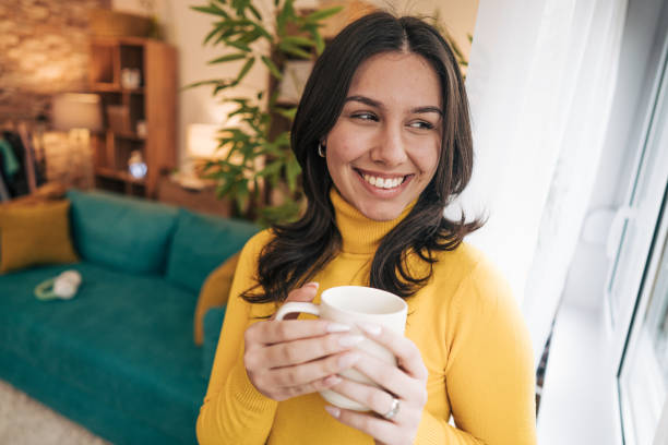 istock A young woman is holding a white mug in her living room while drinking coffee 2190671925