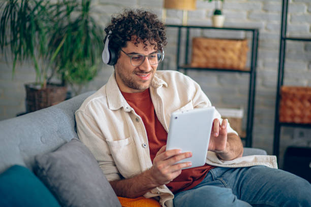istock Happy man with headphones using tablet while relaxing in the couch at home 2190671964