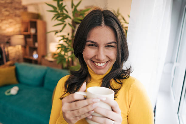 istock A young woman is holding a white mug in her living room while drinking coffee 2190672191