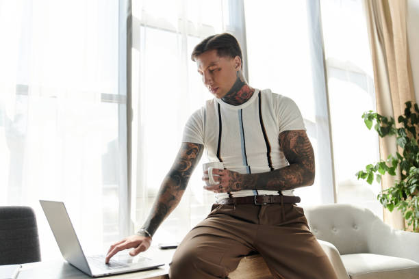istock Young man with tattoos works on laptop while enjoying a cup in bright, modern space 2190672499