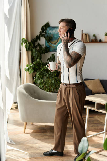 istock Young man with tattoos enjoys coffee while talking on the phone in a stylish room 2190672588