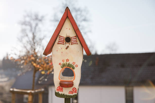 Wooden birdhouse adorned with colorful flowers and whimsical mushrooms, nestled in a serene garden during the quiet winter season