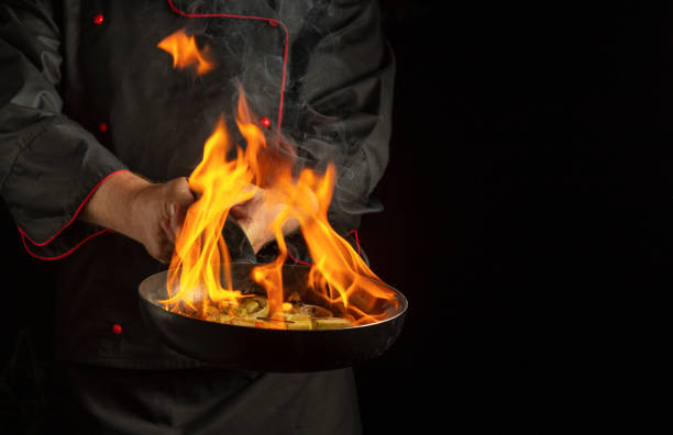 istock In a modern kitchen, a skilled chef expertly tosses sizzling ingredients in a skillet, igniting a spectacular display of flames. The dramatic fire contrasts beautifully with the dark background 2190676950