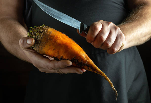 Hands expertly hold a vibrant, freshly harvested carrot ready for slicing, surrounded by a warm, rustic kitchen ambiance. The craft of cooking begins with nature bounty.