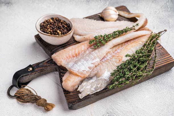 istock fresh Raw Pollock fish fillets on a wooden board with herbs. white background. top view 2190685162