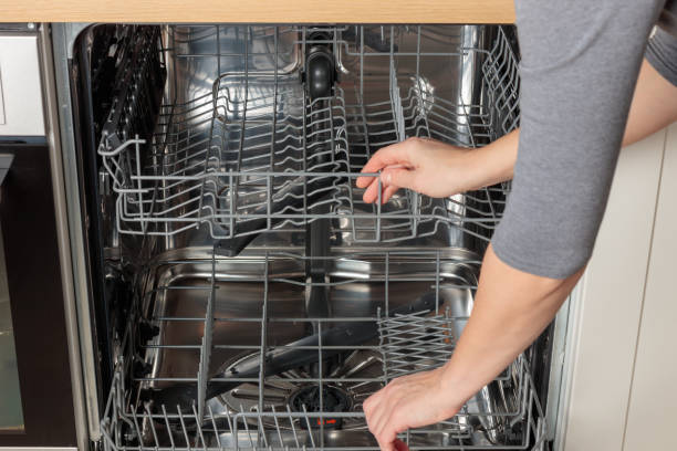 istock Woman hands opening built-in empty dishwasher with its door open. Kitchen with minimalistic white cabinetry at the modern house. 2190689095