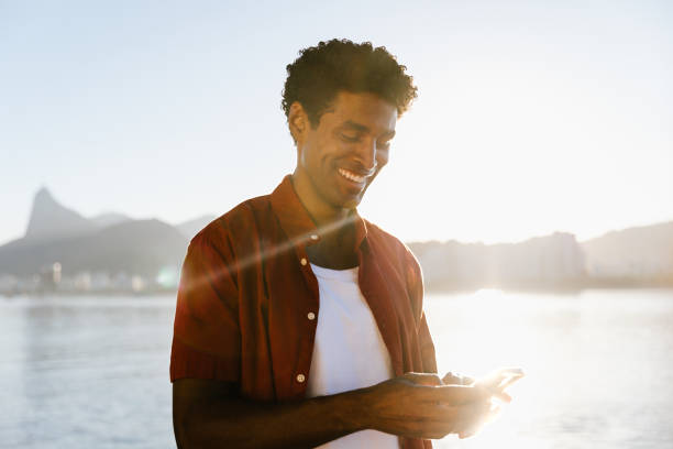 istock Cheerful man texting on smartphone at sunset by the water 2190692423
