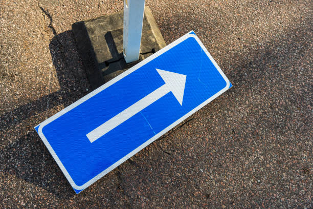 Close-up of blue and white one way road sign with arrow and car parking of castle at Slovenian City of Bled on a blue cloudy summer day. Photo taken August 8th, 2023, Bled, Slovenia.