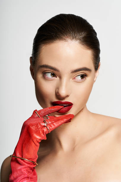 A beautiful young woman poses in a studio, highlighting her bold makeup and stylish accessories.
