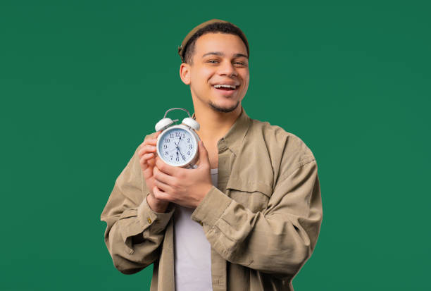 Happy man with alarm clock, green background. Early morning, correct day routine