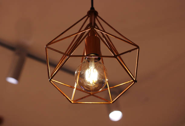 istock Close-up of a modern geometric pendant light with a glowing bulb. Ideal for enhancing interior design, creating a warm and stylish ambiance in living rooms, dining areas, kitchens, or cafes. 2190700151
