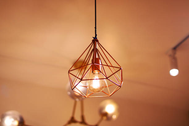 istock Elegant geometric pendant light with a glowing bulb in a copper-colored metal frame, creating a cozy and stylish ambiance. Suitable for modern interiors, cafes, dining rooms, or home decoration. 2190700975
