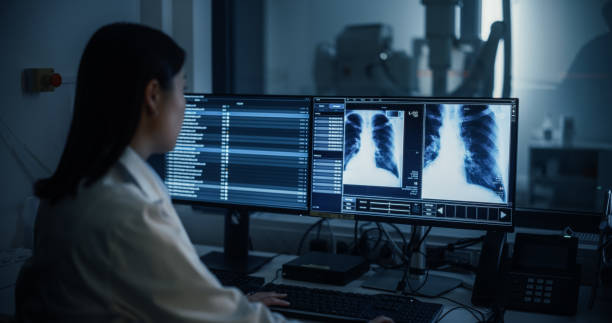 istock Radiologist Analyzing Chest X-rays on Multiple Monitors in a Dark Room. Male Nurse Assisting with Advanced Medical Equipment Visible in Background. Asian Female Doctor Focuses on Detailed Scans 2190716787