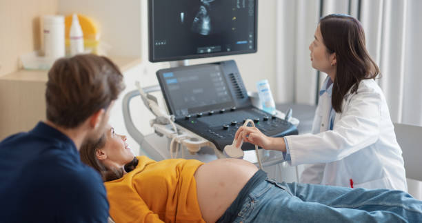 istock Asian Obstetrician Performs Ultrasound on Pregnant Patient, Explaining Baby Development. Modern Medical Equipment Displays Detailed Sonogram Images as Doctor Gestures Towards Screen 2190716935