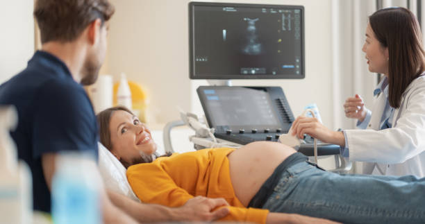 istock Asian Obstetrician Performs Ultrasound on Pregnant Patient, Explaining Baby Development. Modern Medical Equipment Displays Detailed Sonogram Images as Doctor Gestures Towards Screen 2190717066