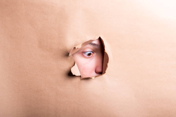 istock Man eye looking through a hole in a sheet of paper. 2190719642