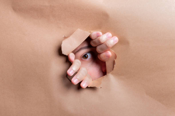 istock Man looking through a paper hole with his hands pushing the paper aside. 2190719645