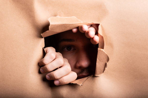 istock Man looking through a paper hole with his hands pushing the paper aside. 2190719658