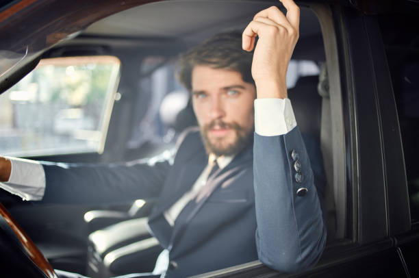 Young businessman wearing a stylish suit and tie, driving a luxury car with a confident smile, holding the steering wheel while looking away from the road ahead