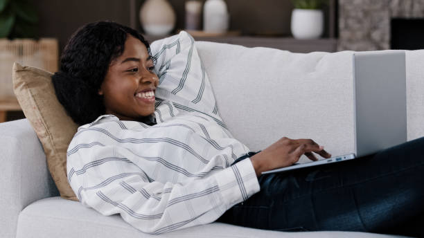 istock Smiling african woman student girl freelancer user lying on couch using laptop typing message online chat with friends happy chatting on computer browsing surfing internet social media freelance work 2190721710