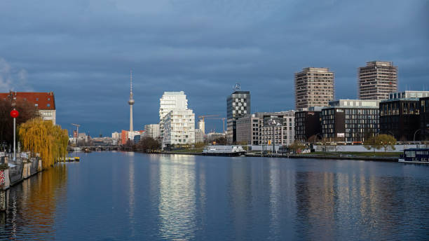Berlin, Germany, 11.11.2024 - serene cityscape seen from Oberbaum Bridge featuring the Spree River, with modern and historical architecture, including Berlin's iconic TV Tower, reflecting on the water under a dramatic cloudy sky