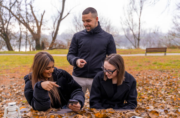 istock small group of young friends having fun using smart phone sitting on a wooden table in a public park in winter 2190728645