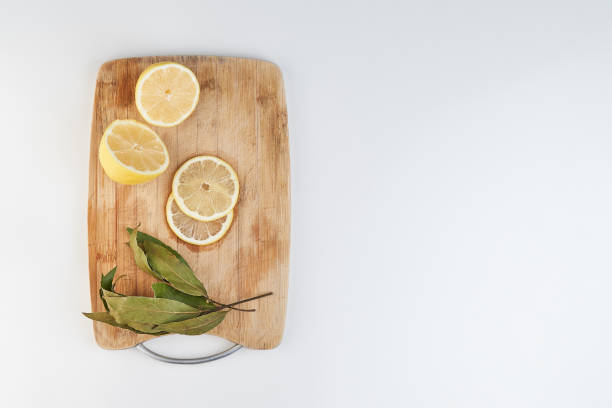 Negative space photograph, from above, of a cutting board with lemon slices and bay leaves. white background
