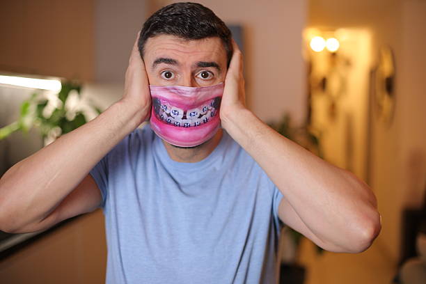 COVID-19, a senior adult man putting on a homemade face mask for Social Distancing. Studio portrait on plain neutral gray background.