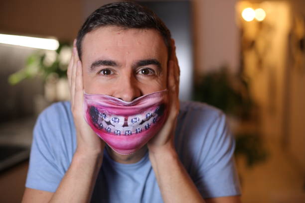 A cute and quite comedic looking Caucasian man in his early forties is playing with  large metallic oral braces. The man is excited to fix his teeth.
